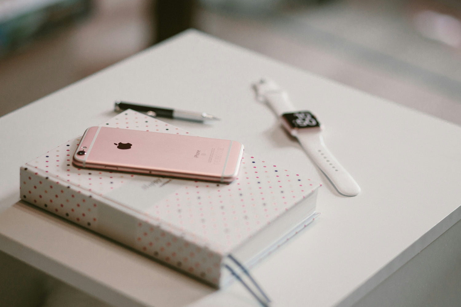 Rose gold phone, white smartwatch, and notebook on a light surface